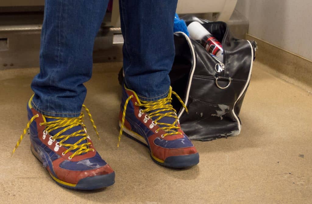 man`s legs with blue trousers and colorful sneakers with untied shoelaces
